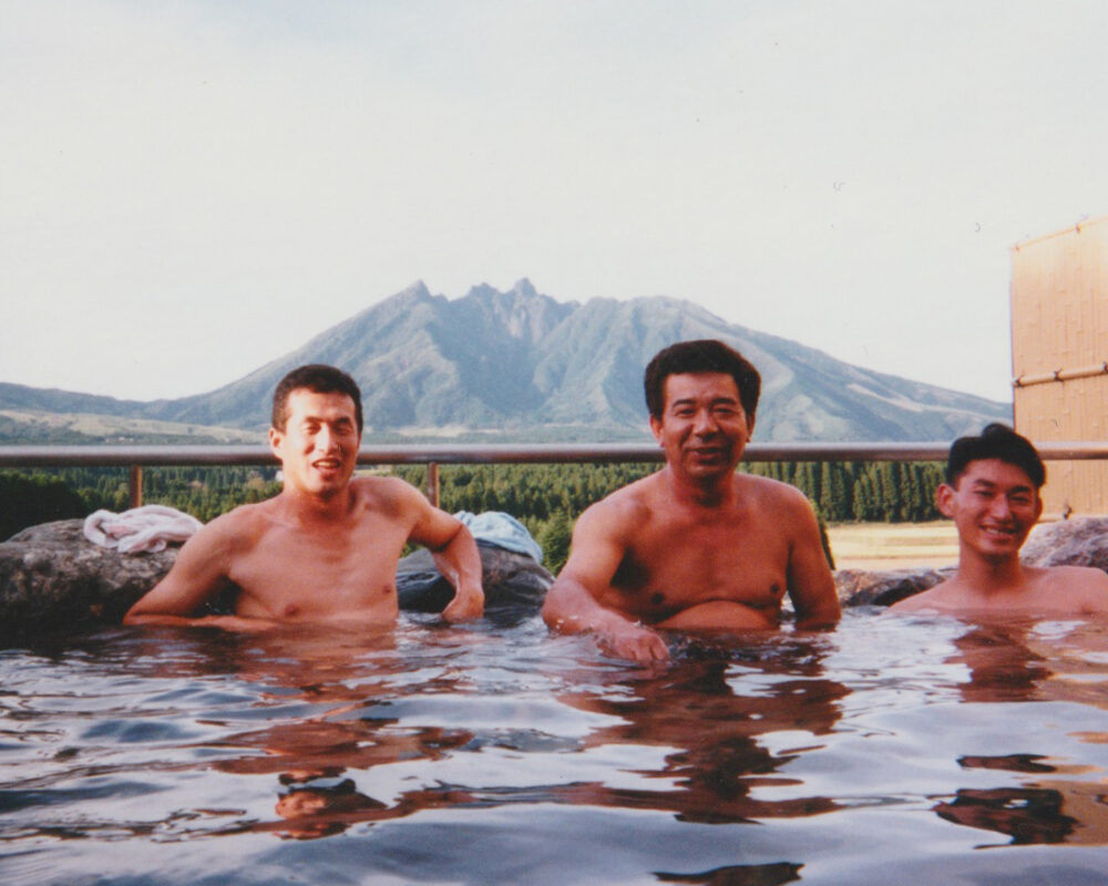 遠くにハッキリとした阿蘇山を背景に、露天風呂でリラックスする小野先生と仲間たち